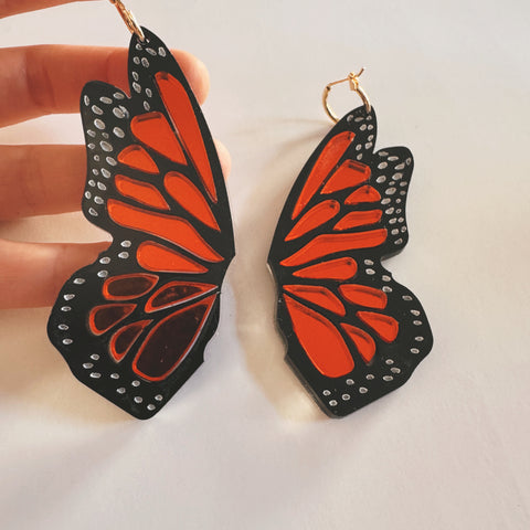 Butterfly wing earrings held by a hand on a light background