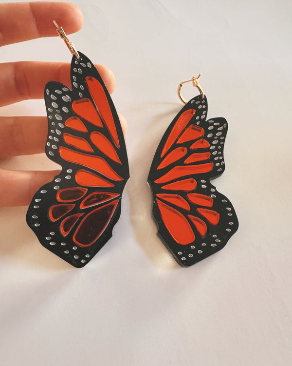 Butterfly wing earrings held by a hand on a light background