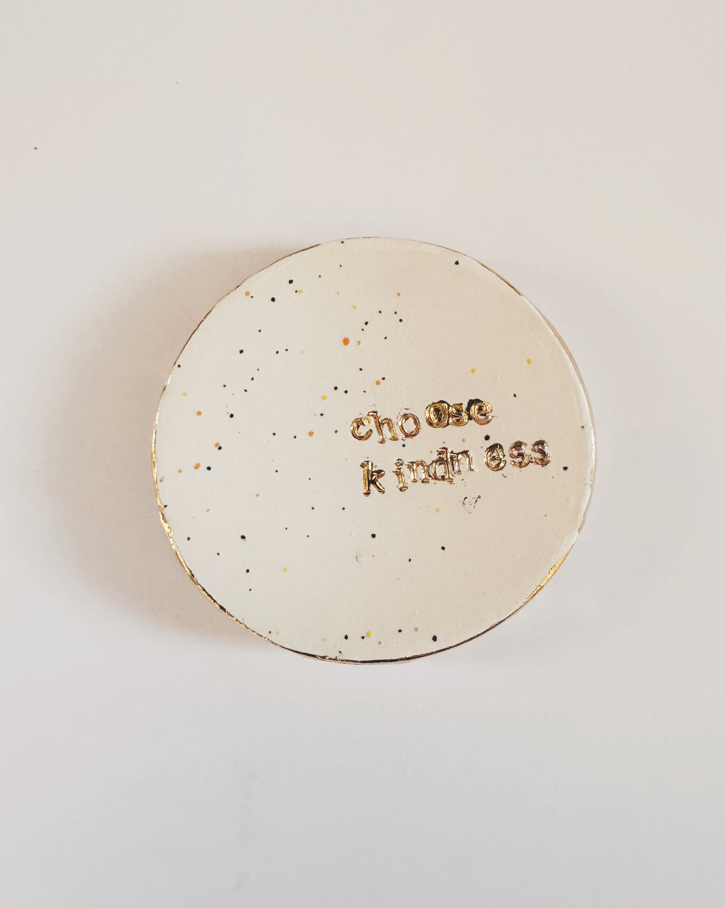 Round speckled ceramic dish with 'Choose Kindness' text held by a hand on a light background