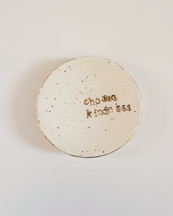 Round speckled ceramic dish with 'Choose Kindness' text held by a hand on a light background