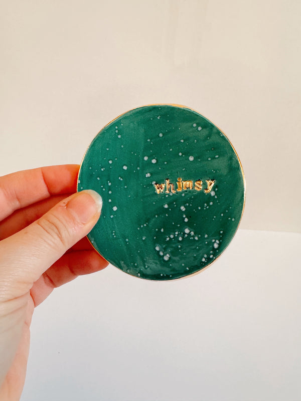 Hand holding a green round product with 'whimsy' branding against a beige background